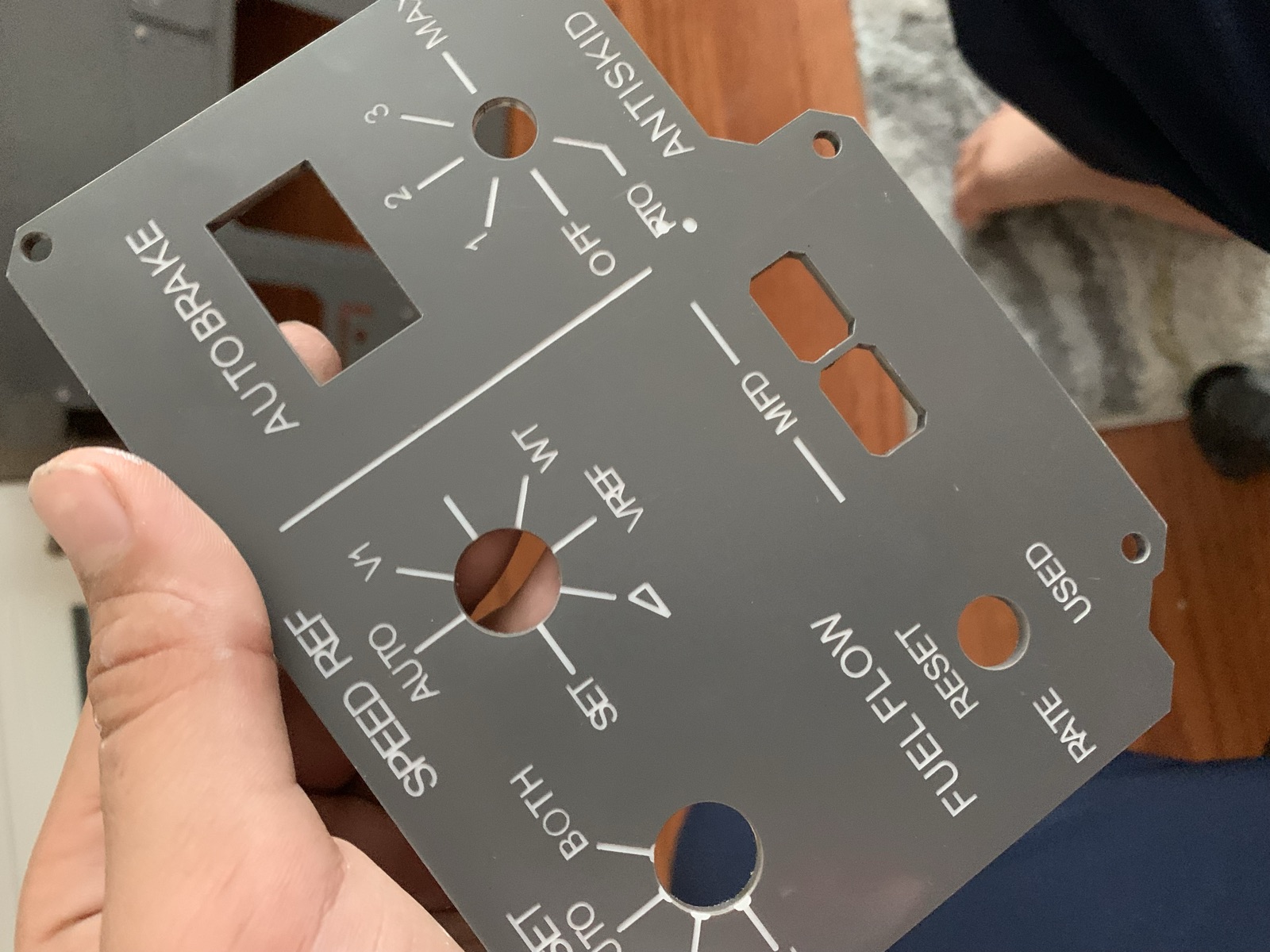 Dark gray laser cut panel held in hand showing speed ref, autobrake, antiskid, and fuel flow labels with cut openings