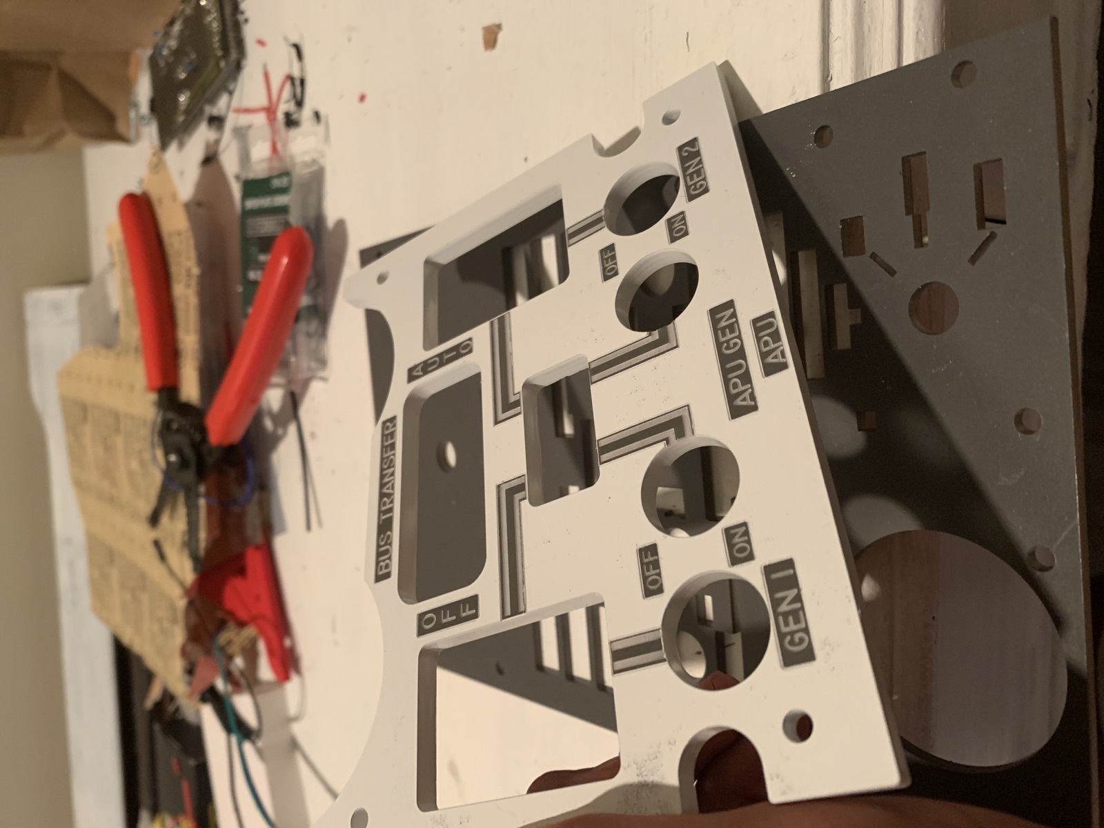 Cut white bus panel held over a darker sub plate with wiring and tools nearby